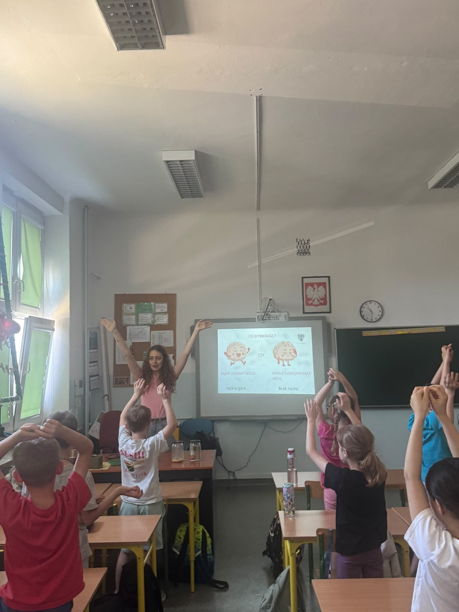 Dzieci i prowadząca podnoszą ręce podczas wspólnego ćwiczenia ruchowego